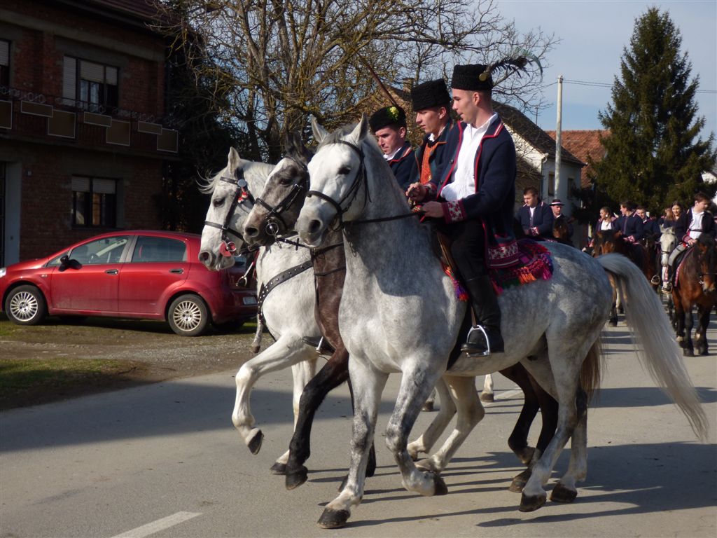 Jahači u tradicionalnim nošnjama jašu sive konje niz seosku cestu